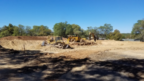 A group of construction vehicles are parked in the dirt.